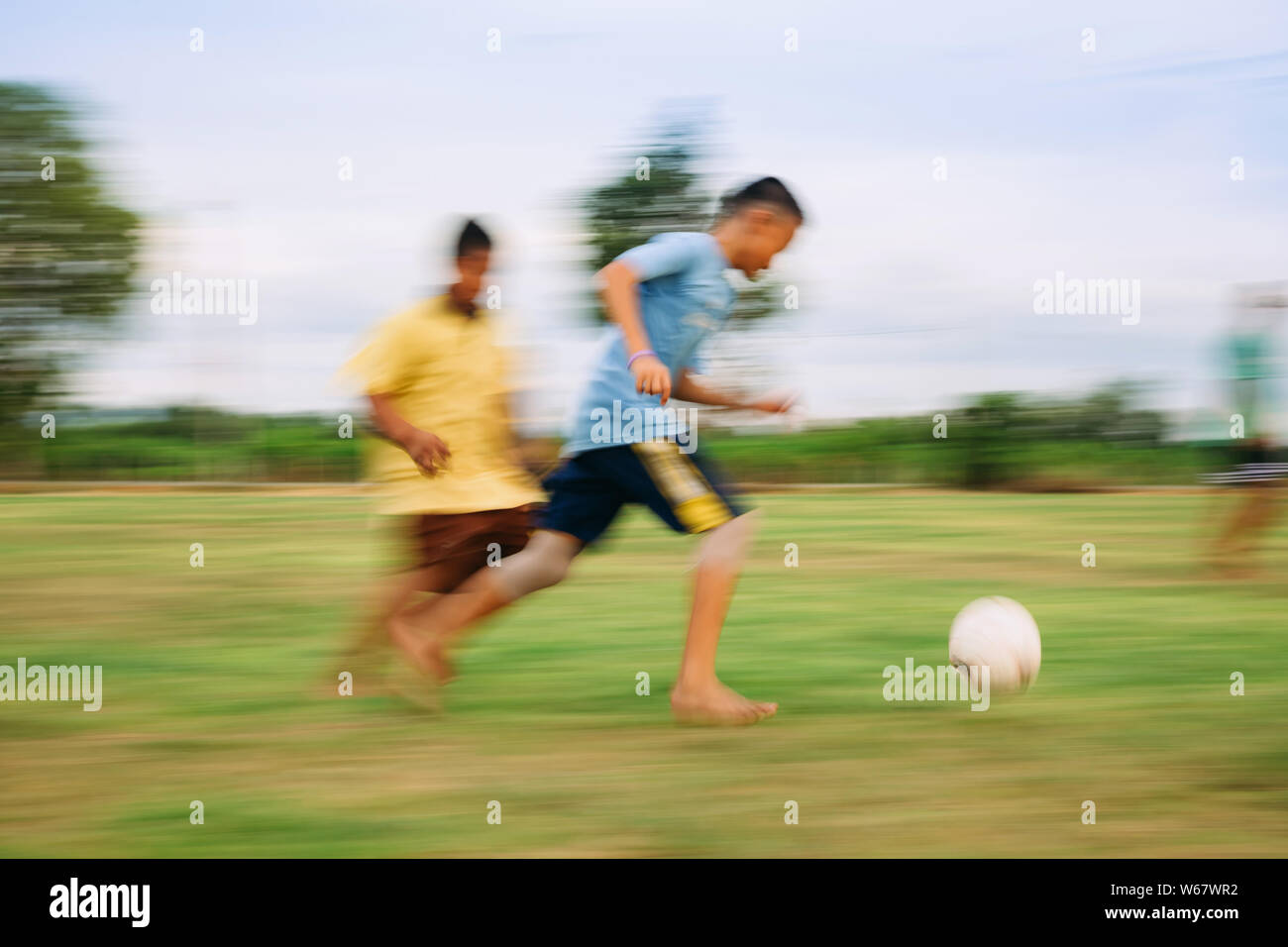 Speed motion blur picture of kids having fun playing soccer football for exercise in community rural area. Concept for sport background with anonymous Stock Photo