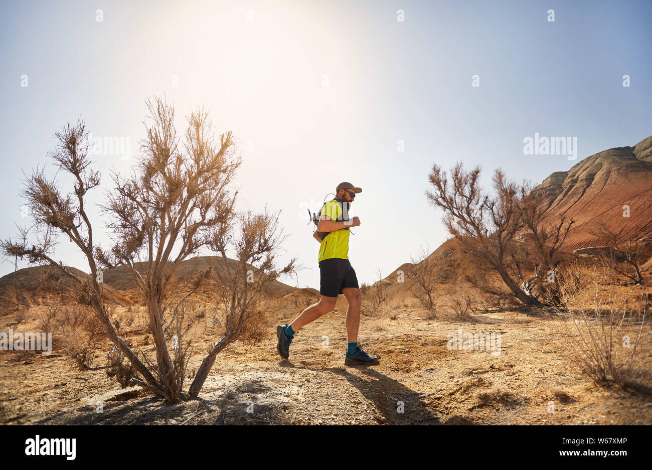 Runner athlete with beard running on the wild trail at red mountains in the desert Stock Photo