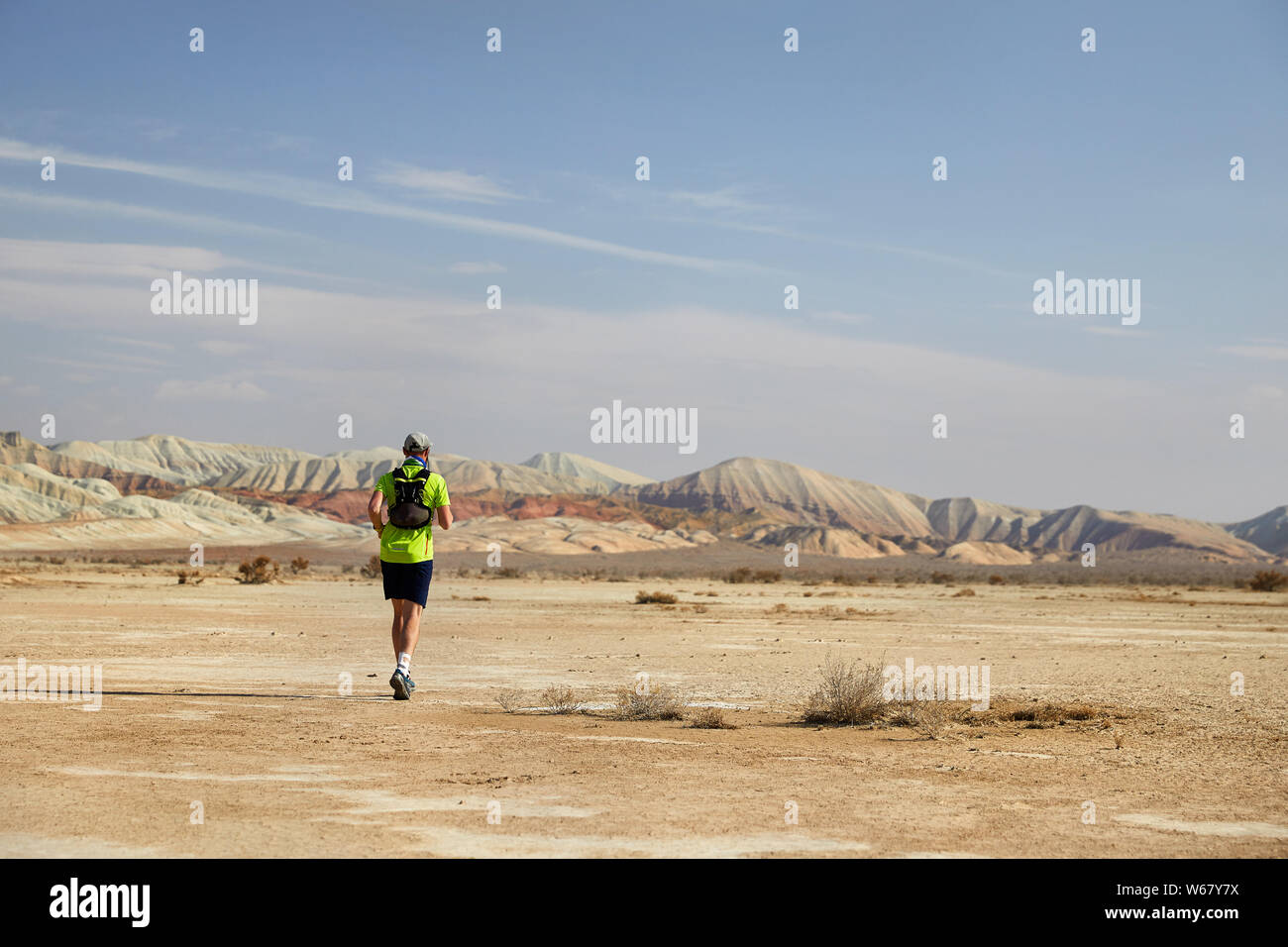 Runner athlete with backpack running on the wild trail at red mountains in the desert Stock Photo