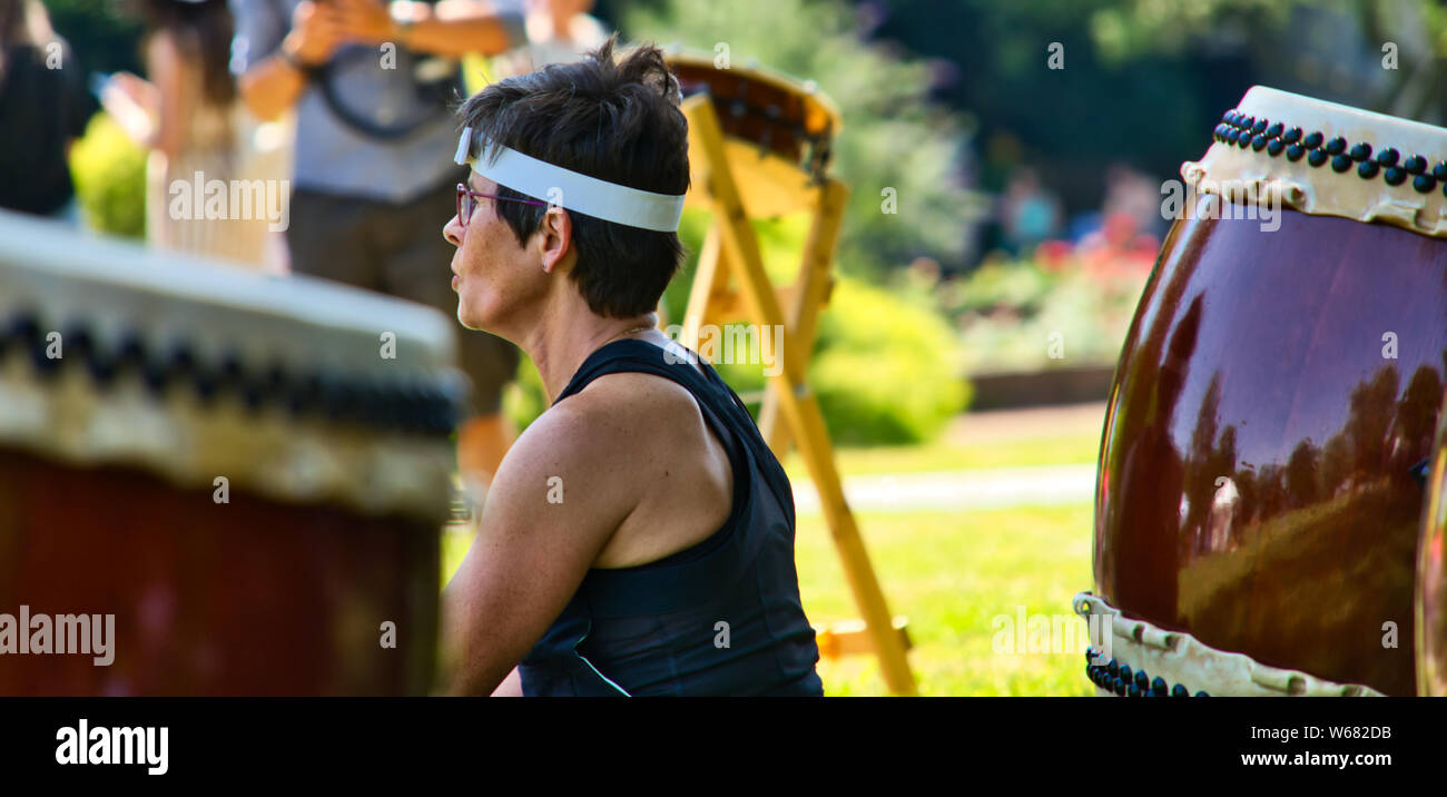 Hannover, Germany, June 30., 2019: medium Old Taiko drummer sits on the lawn in front of her drum and beats the instrument during a performance in a p Stock Photo
