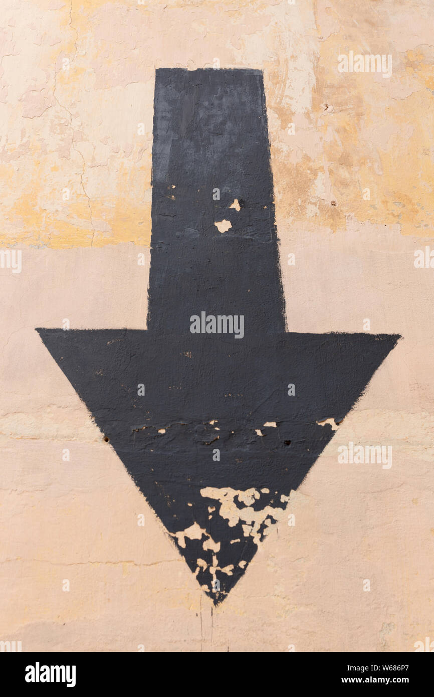 Black aged arrow on concrete wall pointing down Stock Photo