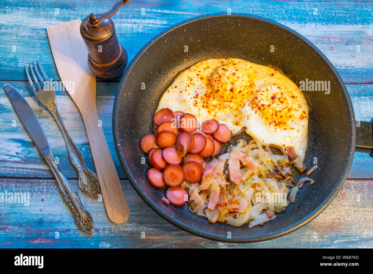 Scrambled eggs with bacon, onion and sausage. In the pan on the table. Stock Photo