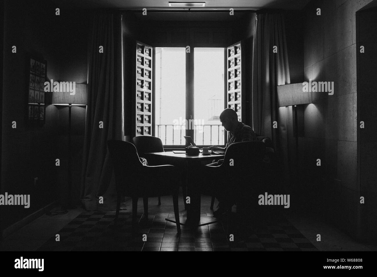 Black and white silhouette shot of a male sitting on a chair around the table near an open window Stock Photo