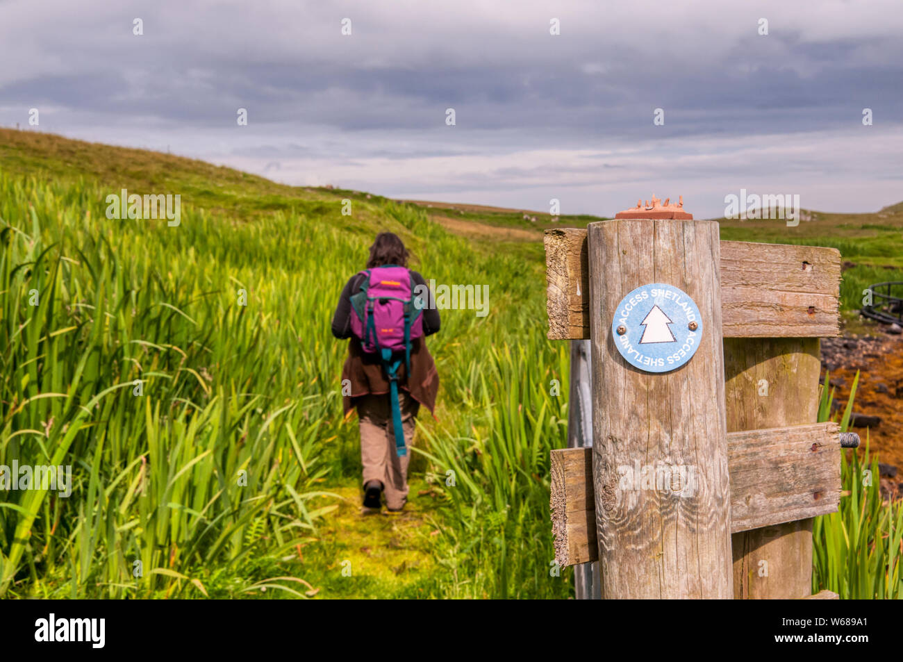 A walker near Burravoe on the island of Yell, Shetland, passes an Access Shetland waymarking sign. Stock Photo