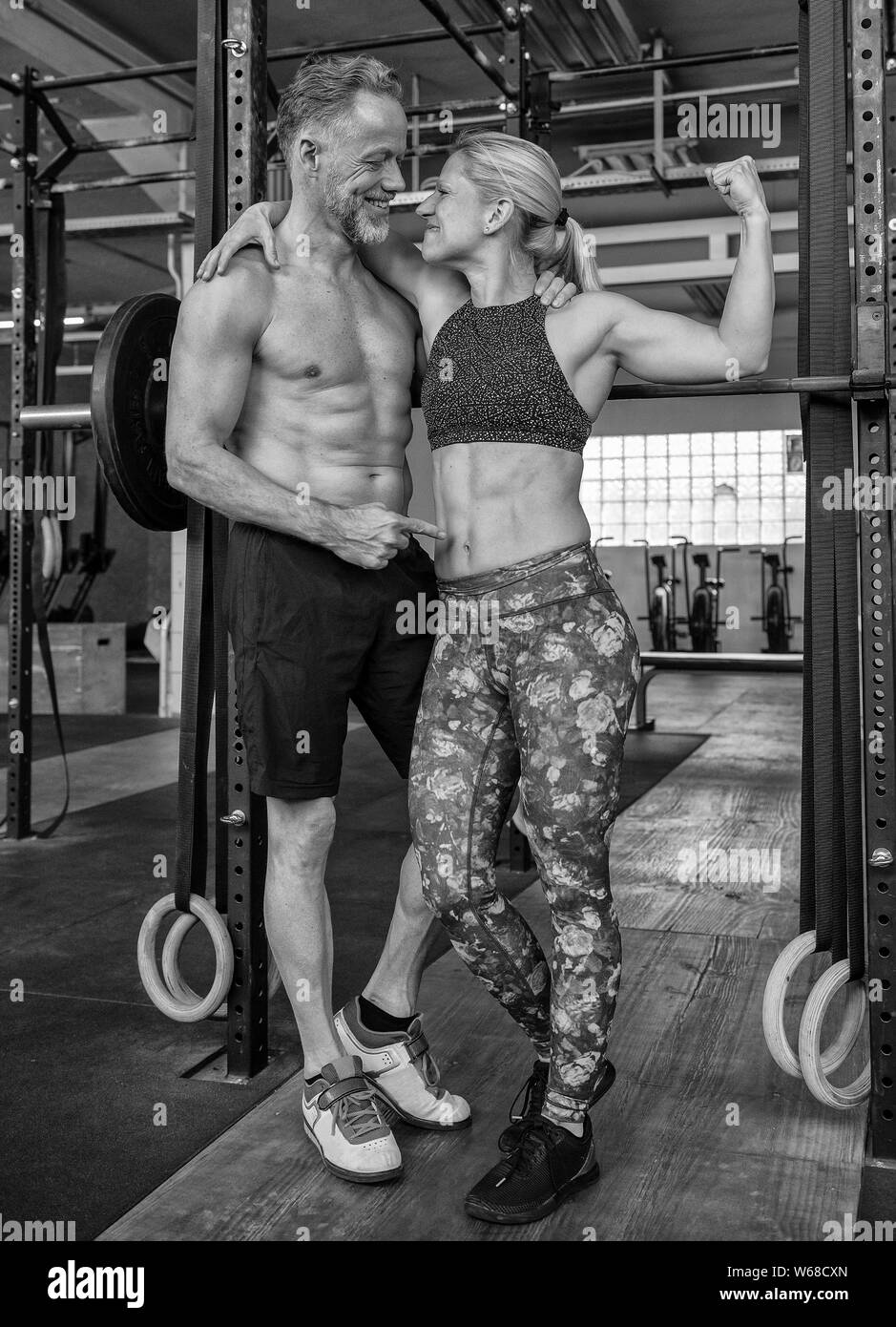 Portrait of a middle aged attractive and athletic couple who is looking at each other and having fun. Strong man and woman in a gym. Black and white. Stock Photo