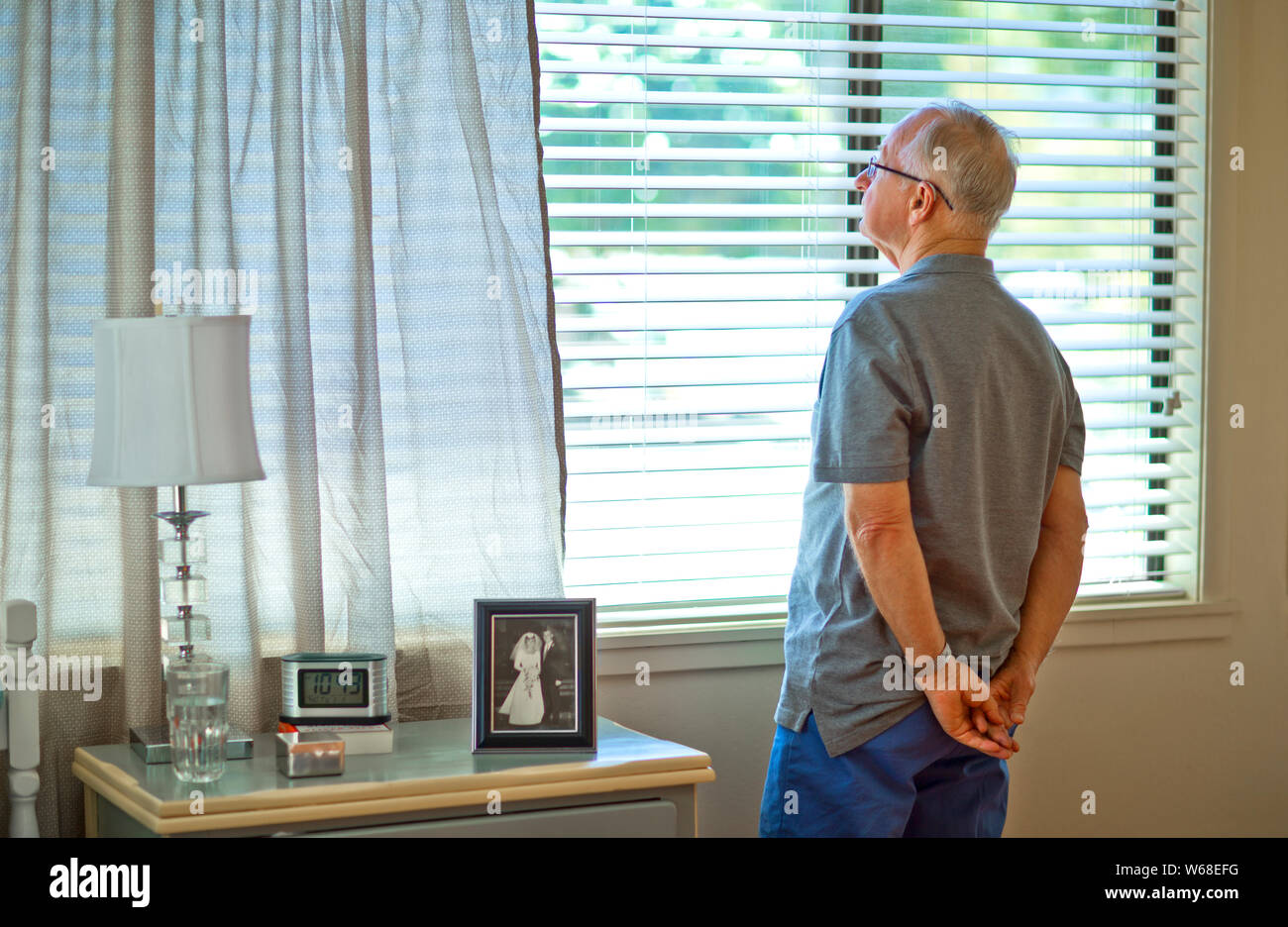 Thoughtful senior man gazing out the window of his rest home bedroom. Stock Photo