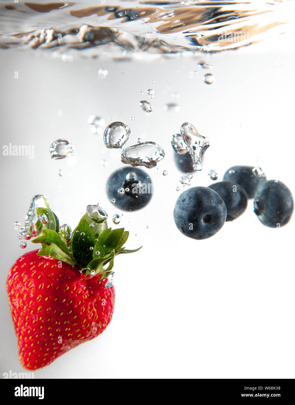 A strawberry and some blueberries fall into water creating beautiful