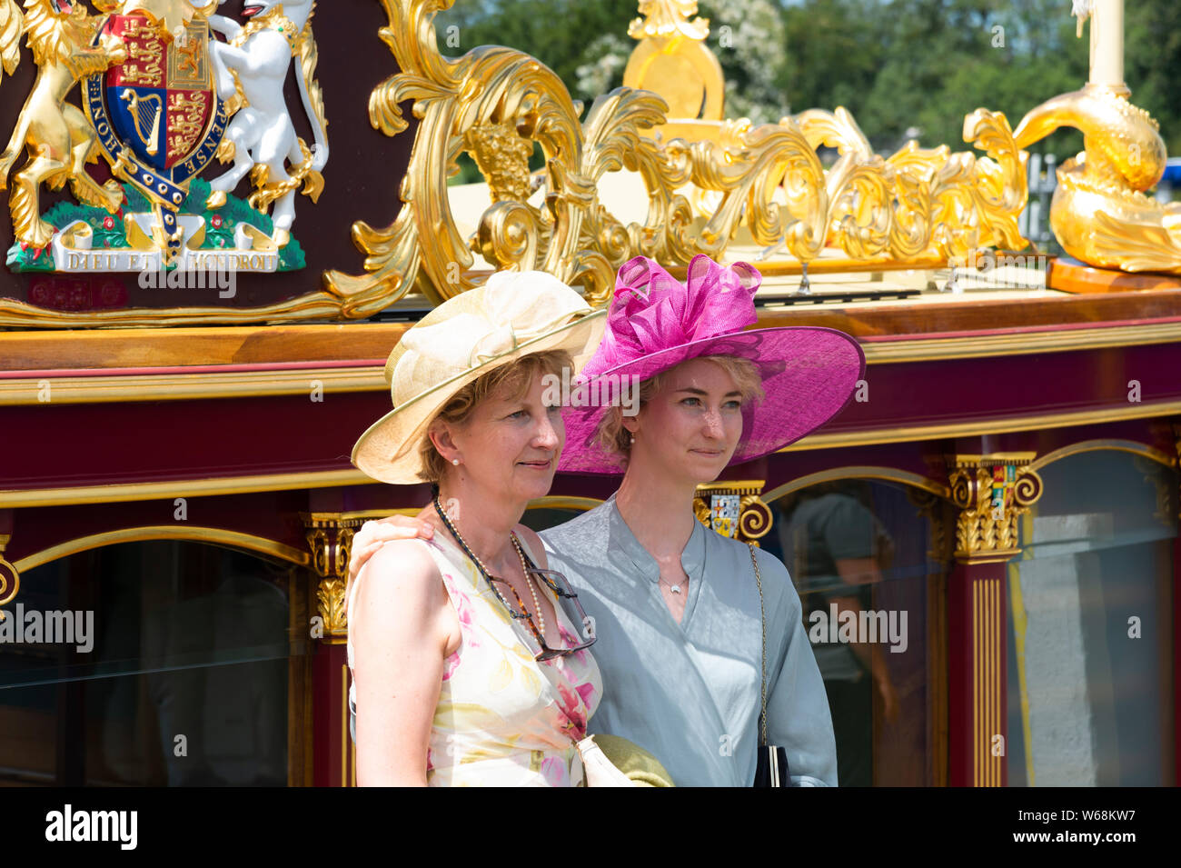 Two women wearing hats standing beside Gloriana the Queen's golden