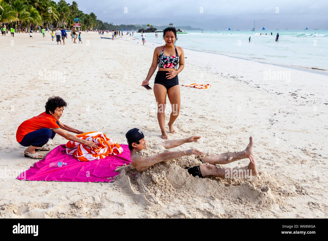 Tourists Being Covered In Sand, White Beach, Boracay, Aklan Province, The Philippines. Stock Photo