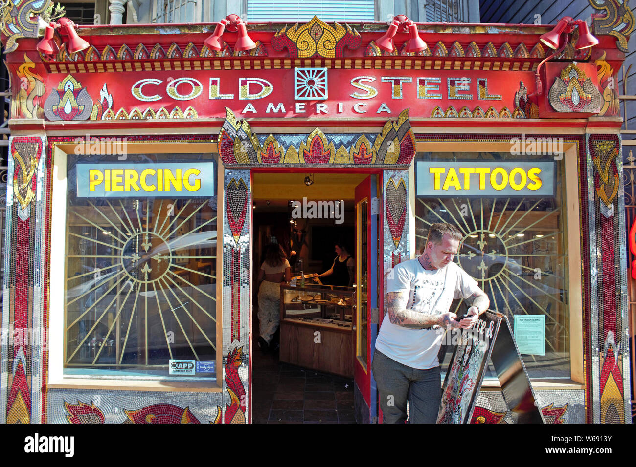 Man checks his phone in front of a piercing and tattoo parlor. Stock Photo