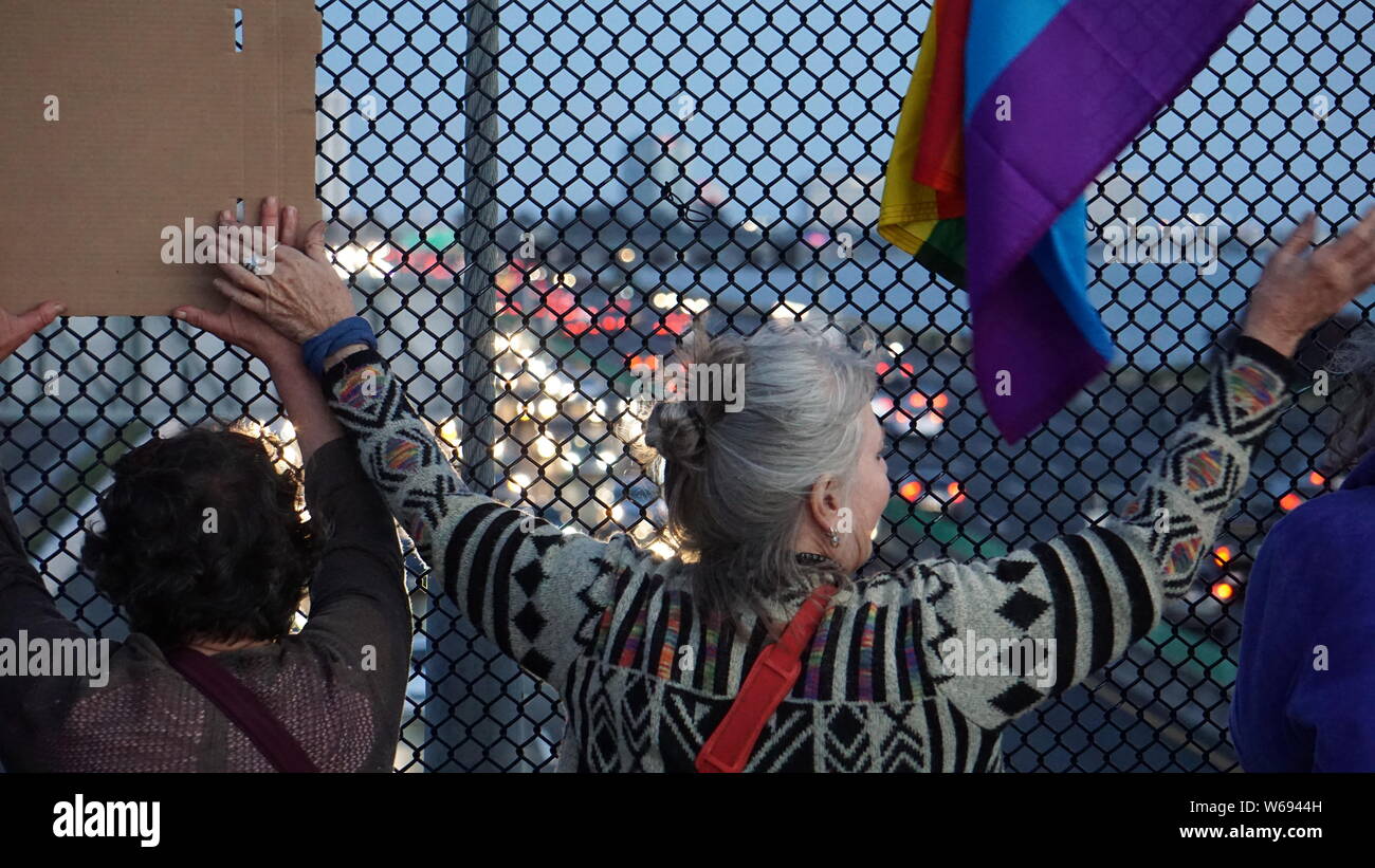 Protestors holding hands on the Berkeley Pedestrian Bridge over Highway 80 with rainbow flag. Lights For Liberty vigil to protest US detention camps. Stock Photo