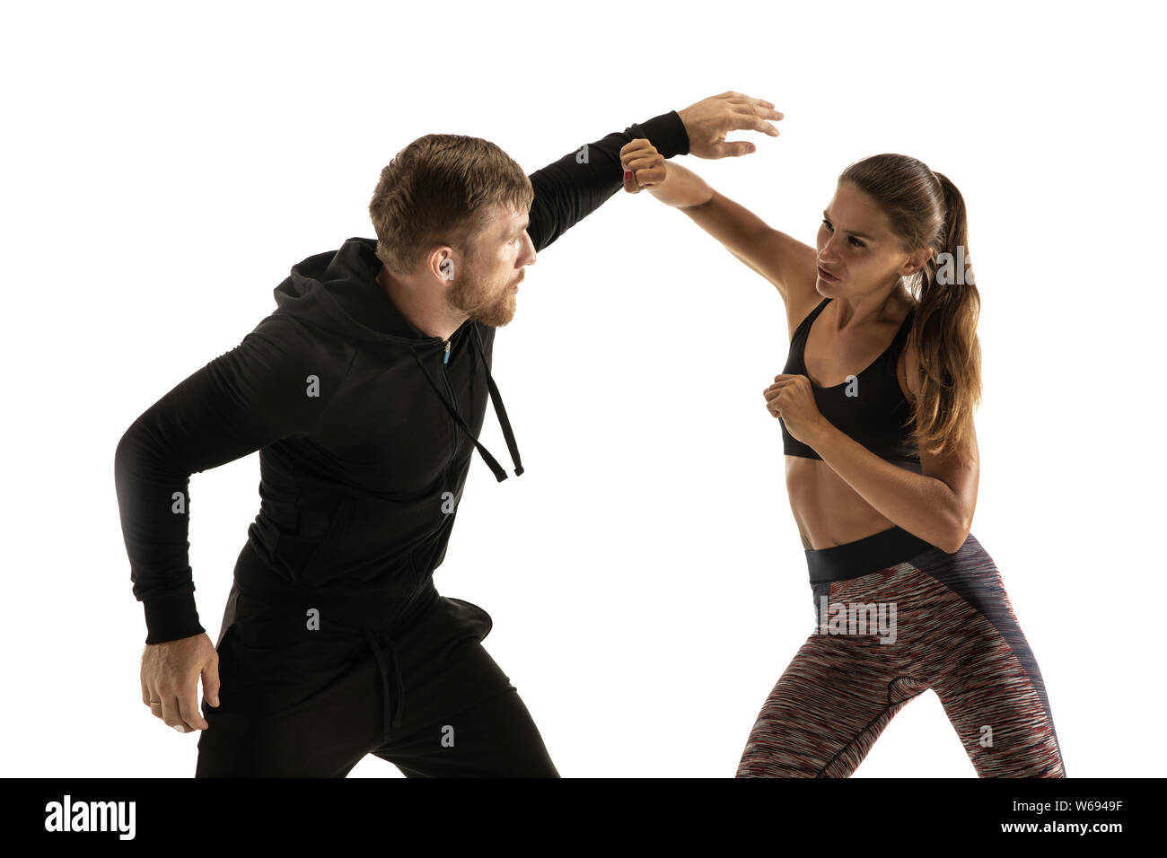 Man in black outfit and athletic caucasian woman fighting on white studio background. Women's self-defense, rights, equality concept. Confronting domestic violence or robbery on the street. Stock Photo