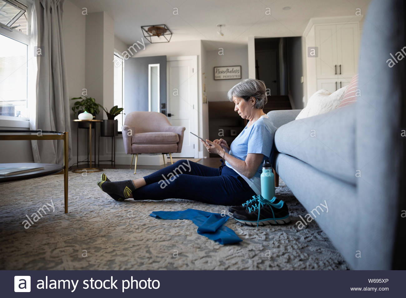 Senior woman with digital tablet preparing to exercise on living room floor Stock Photo