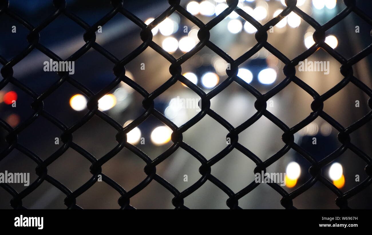 Highway 80W from Berkeley Pedestrian Bridge.  White oncoming car headlights at night in soft focus behind chain link fence. Stock Photo
