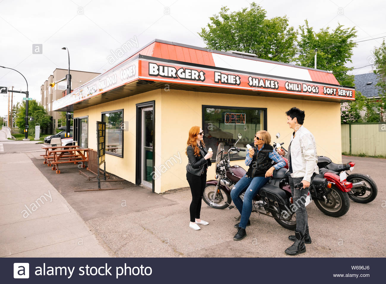 Women friends eating ice cream on motorcycles in parking lot of drive