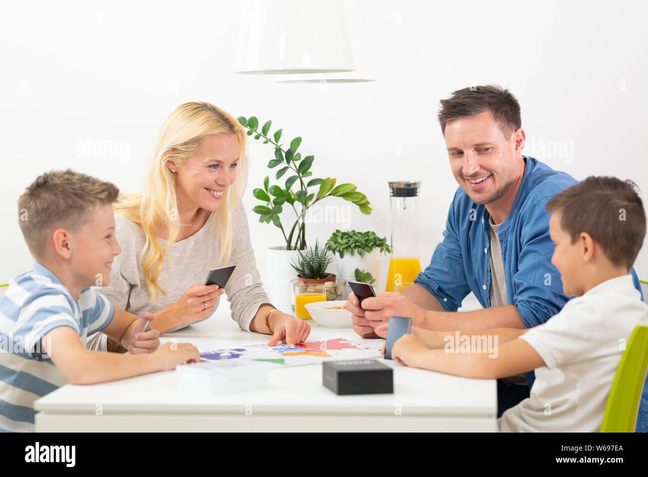 Happy young family playing card game at dining table at bright modern home. Stock Photo