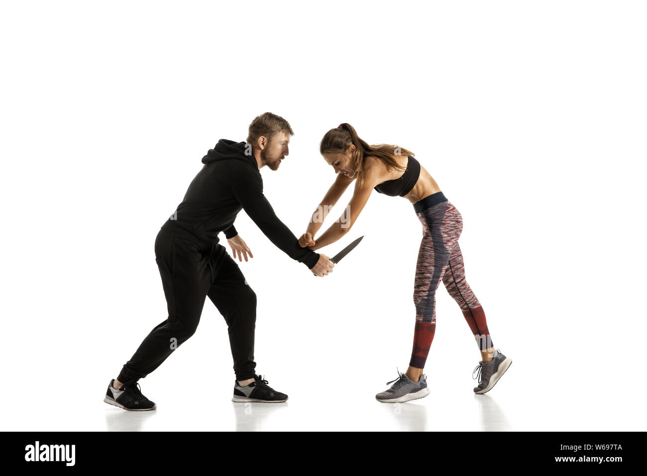 Man in black outfit and athletic caucasian woman fighting on white studio background. Women's self-defense, rights, equality concept. Confronting domestic violence or robbery on the street. Stock Photo