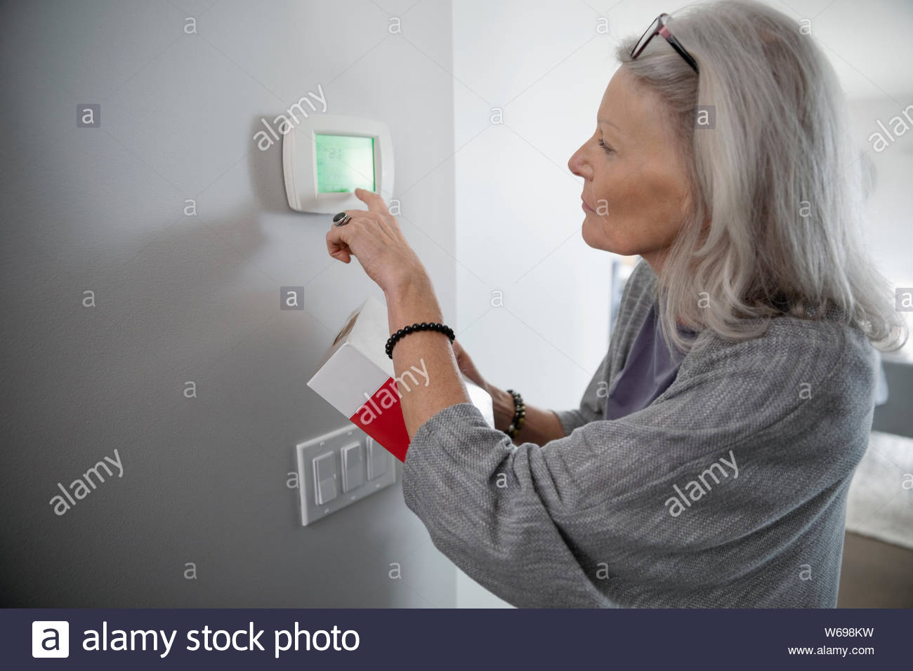 Senior woman programming digital thermostat Stock Photo
