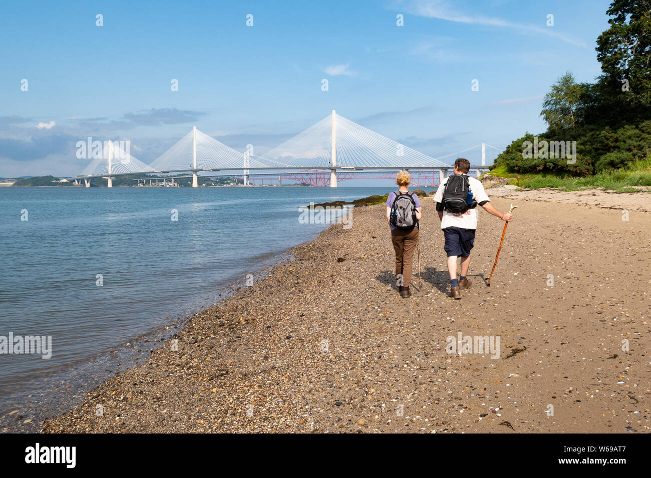 John Muir Way long distance walk - couple walking on beach towards the Queensferry Crossing bridge, Scotland, UK Stock Photo