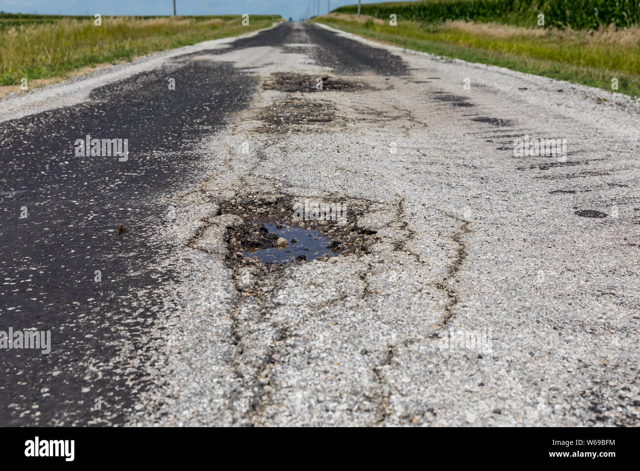 Pothole with water and cracks in a rural country road Stock Photo