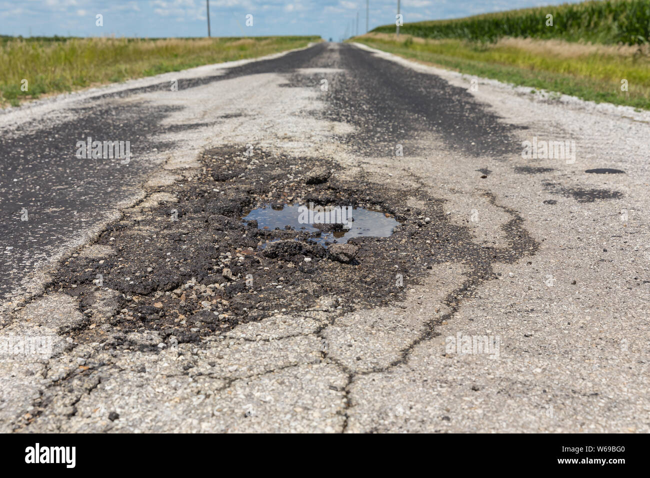 Pothole with water and cracks in a rural country road Stock Photo