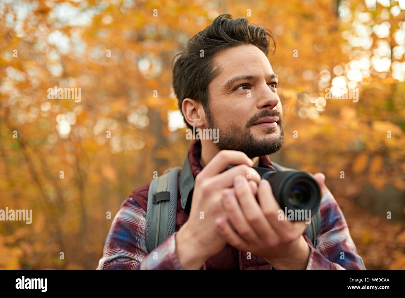 Attractive caucasian man taking pictures with a mirrorless camera through the forest in the fall in Canada Stock Photo