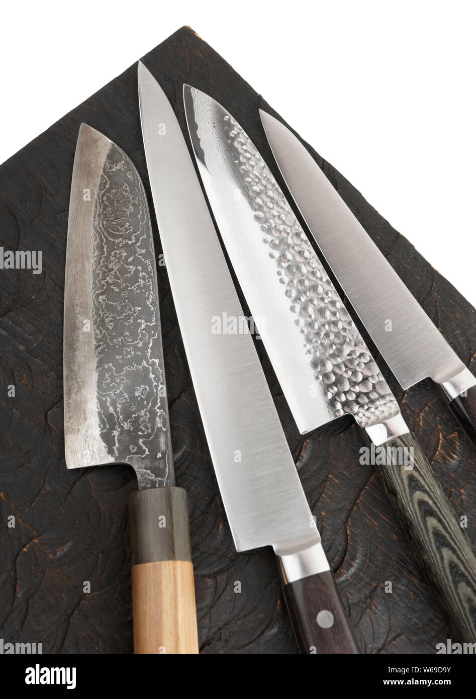 Four different knives on black wooden board, fragment Stock Photo