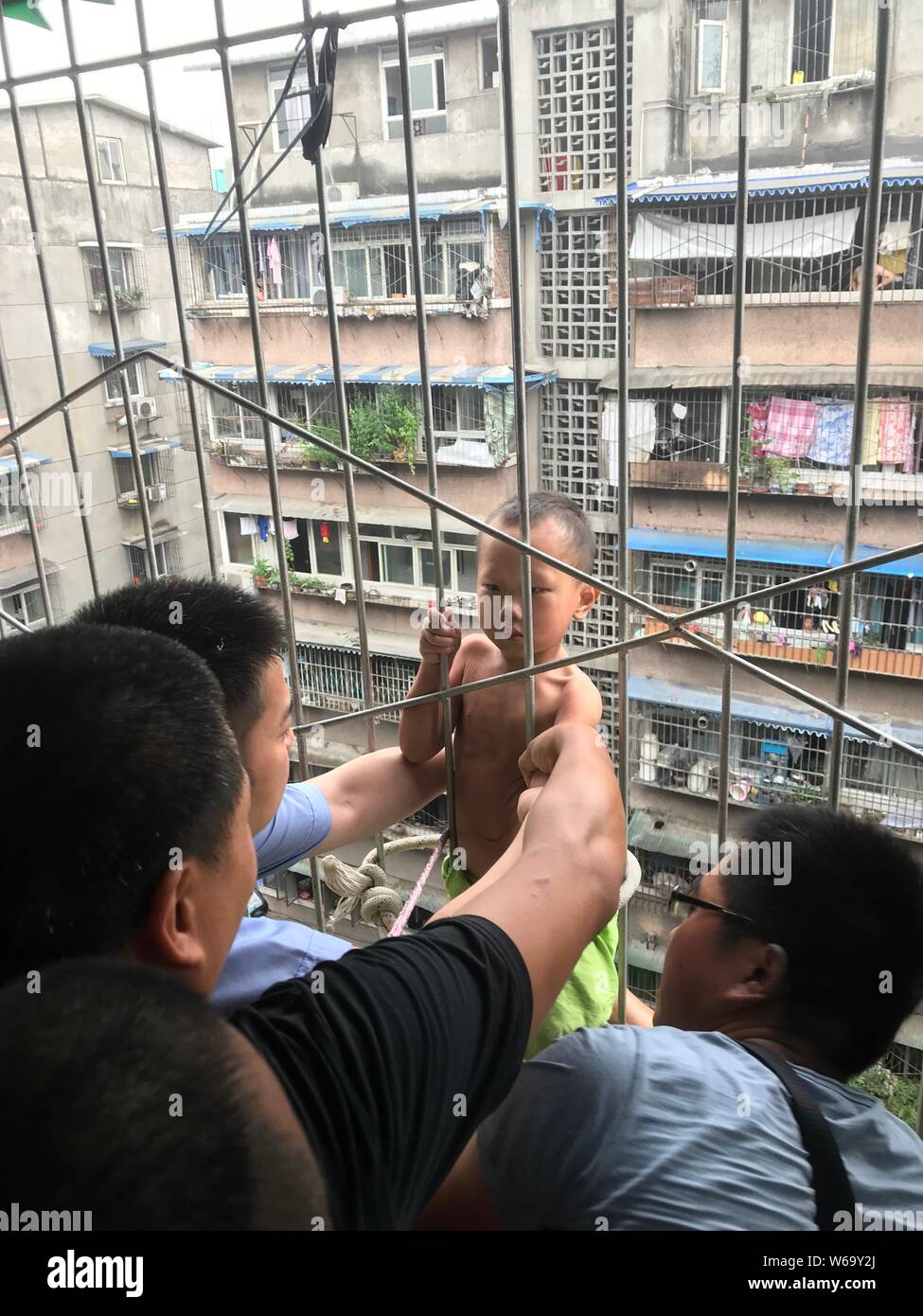 Police officers try to rescue a 4-year-old boy as he clings to the bars of a seventh storey apartment window after falling from the eighth floor in Ch Stock Photo