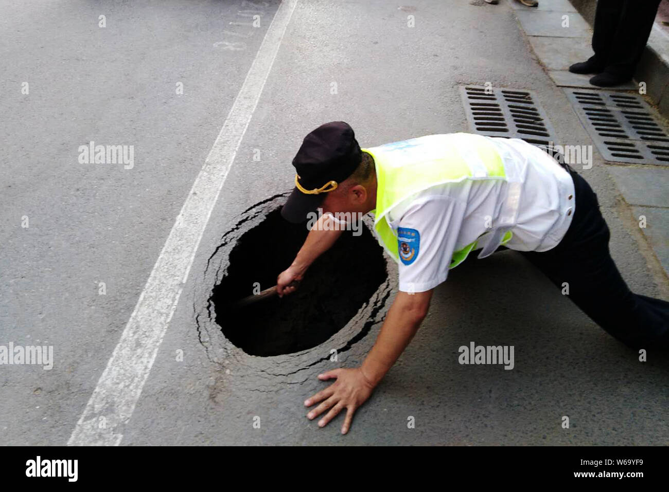 A Chinese auxiliary traffic police officer checks a sinkhole in a cordoned-off area on a street in Zhengzhou city, central China's Henan province, 4 J Stock Photo