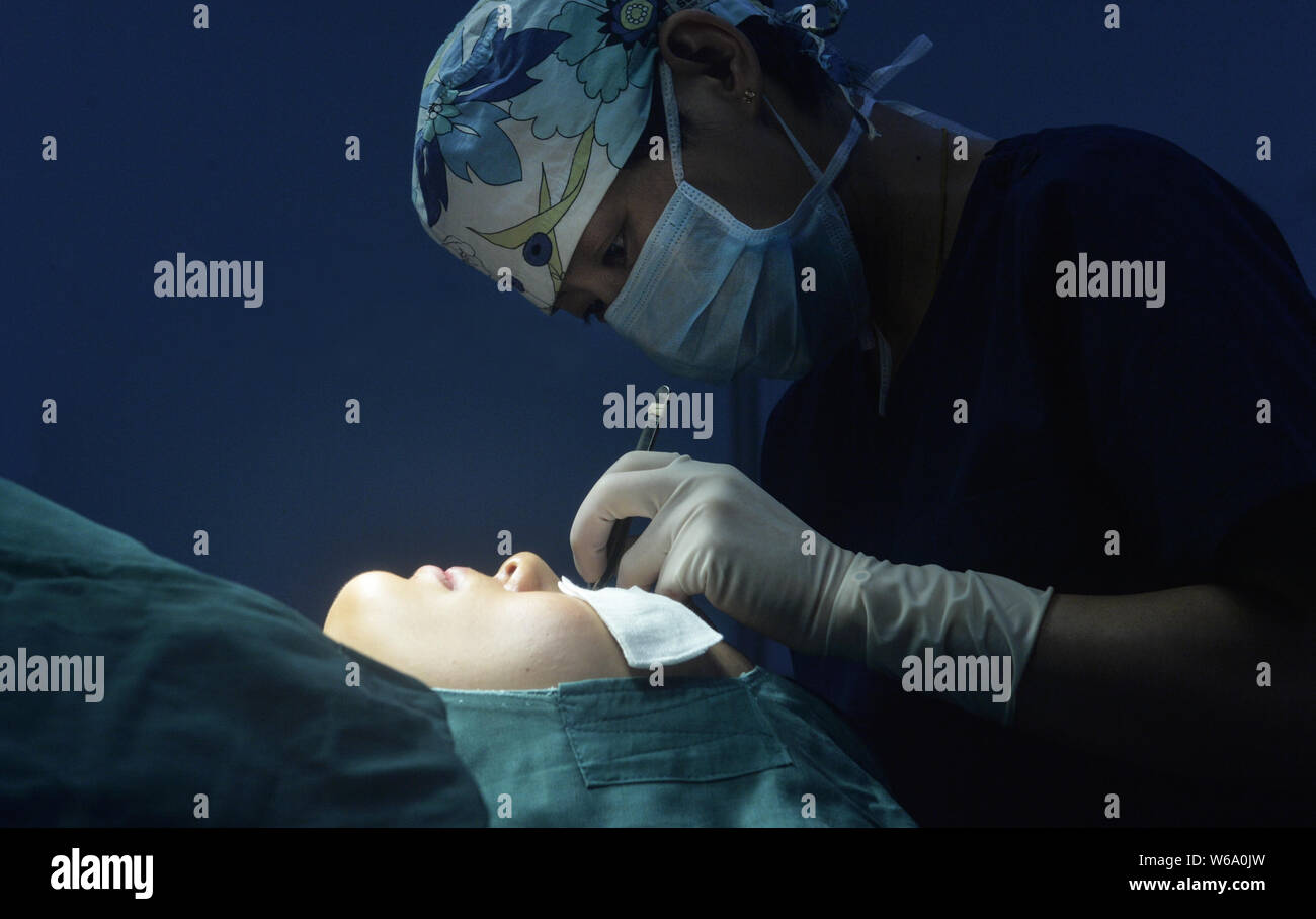 A doctor performs a cosmetic surgery on the eyes of a female young