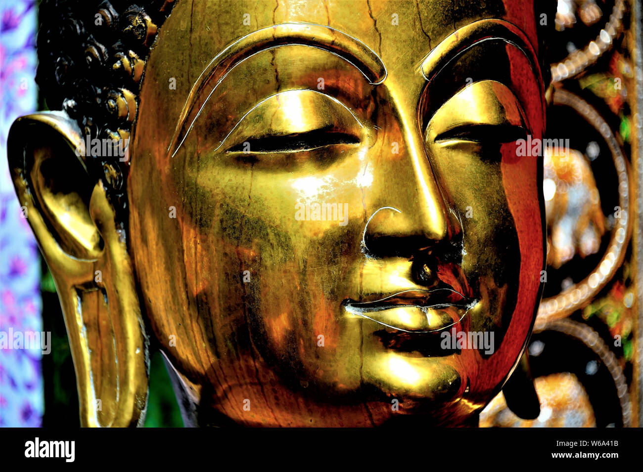 Close up of brass statue of Buddha showing face with calm expression and rich metallic tones and textures Stock Photo