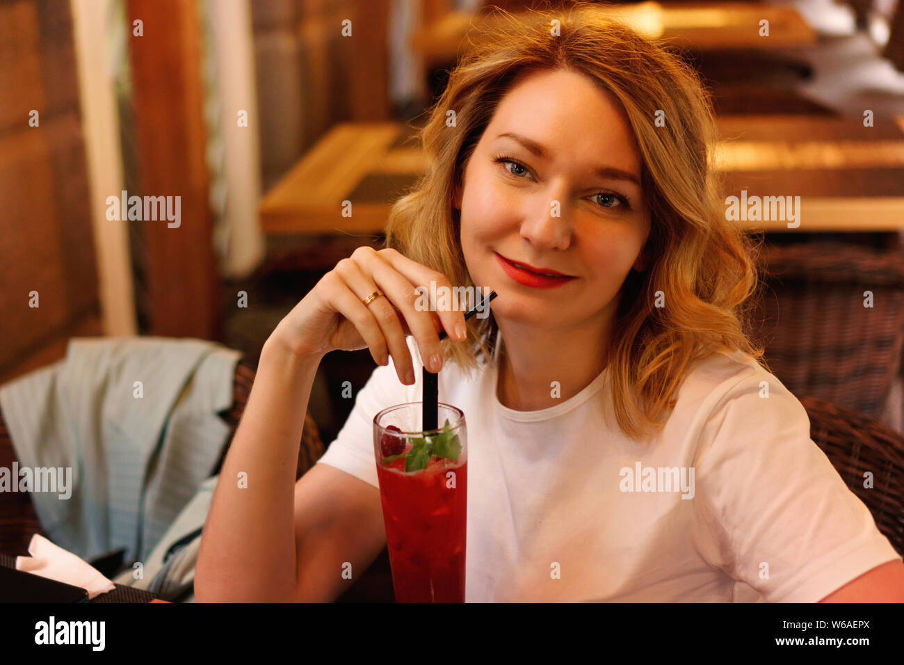 Closeup portrait of an attractive girl on summer terrace of restaurant. She is enjoying a cool drink and looking into camera. Summer holiday concept Stock Photo