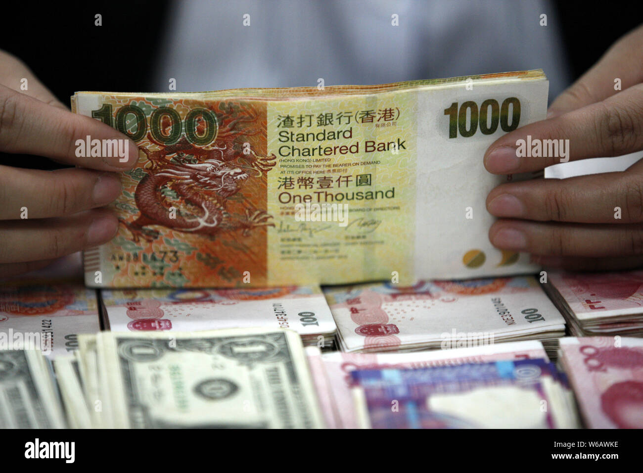 FILE--A Chinese clerk counts Hong Kong dollar (HKD) banknotes over RMB ( renminbi) yuan notes and US dollar notes at a bank in Huaibei city, east  Chi Stock Photo - Alamy