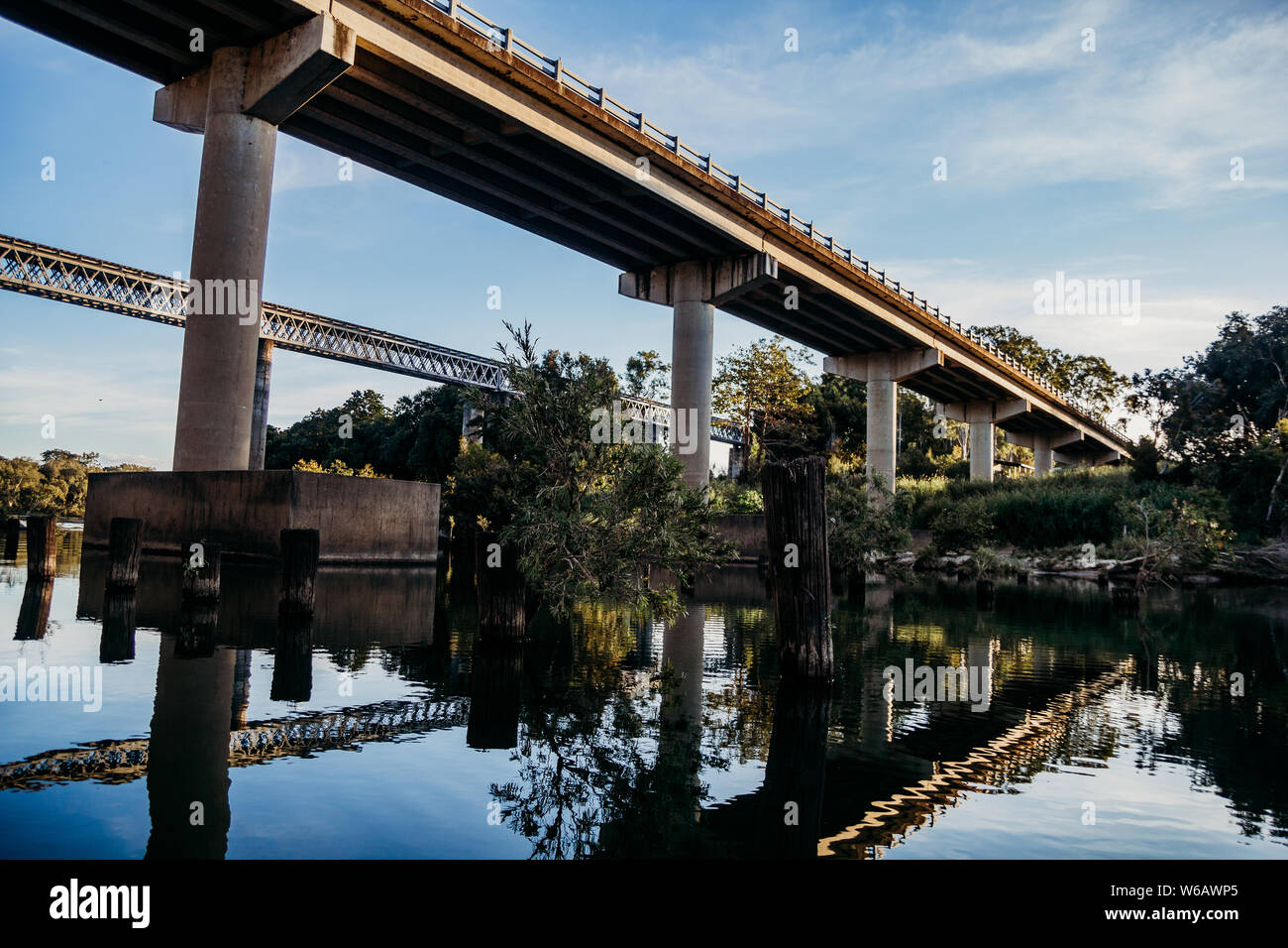 Two bridges and surrounding trees and bushes reflect into the still river water. Stock Photo