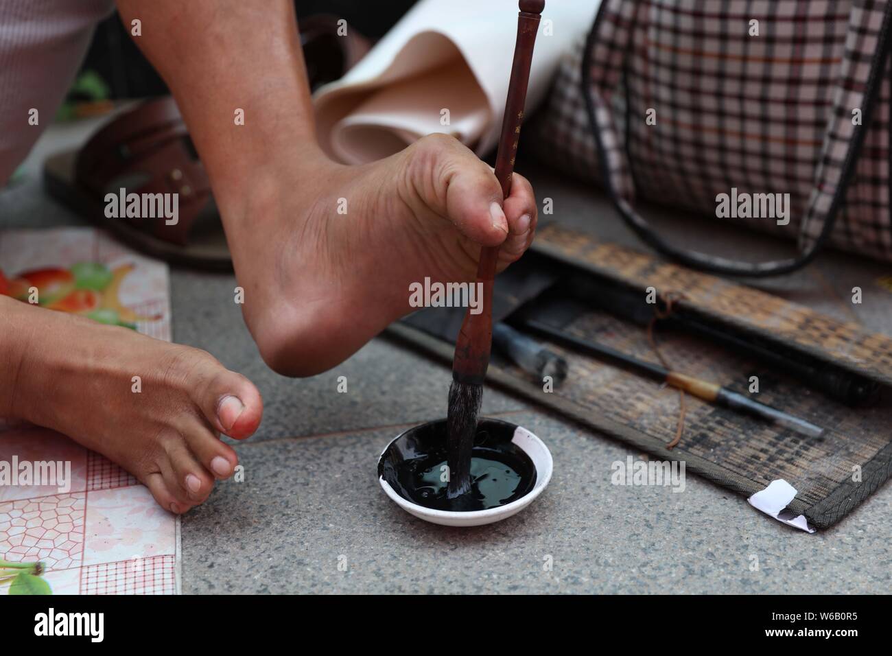 The handicapped Chinese man without hands uses his toes to write calligraphy of 'Zi Qiang Bu Xi', which means 'striving constantly for self-improvemen Stock Photo