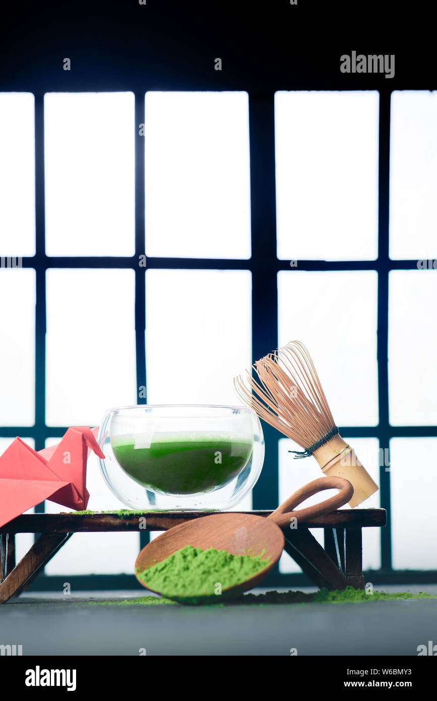 Matcha green tea in a double wall glass tea bowl with a bamboo whisk and a red origami crane