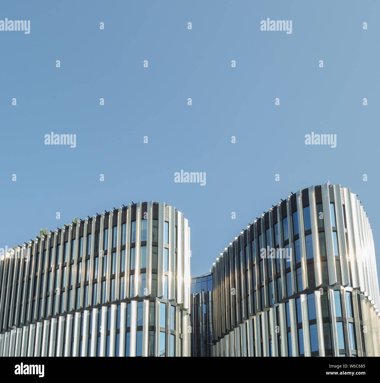 A wavy modern building reflecting sunlight on cloudless plain blue sky as a simple background Stock Photo