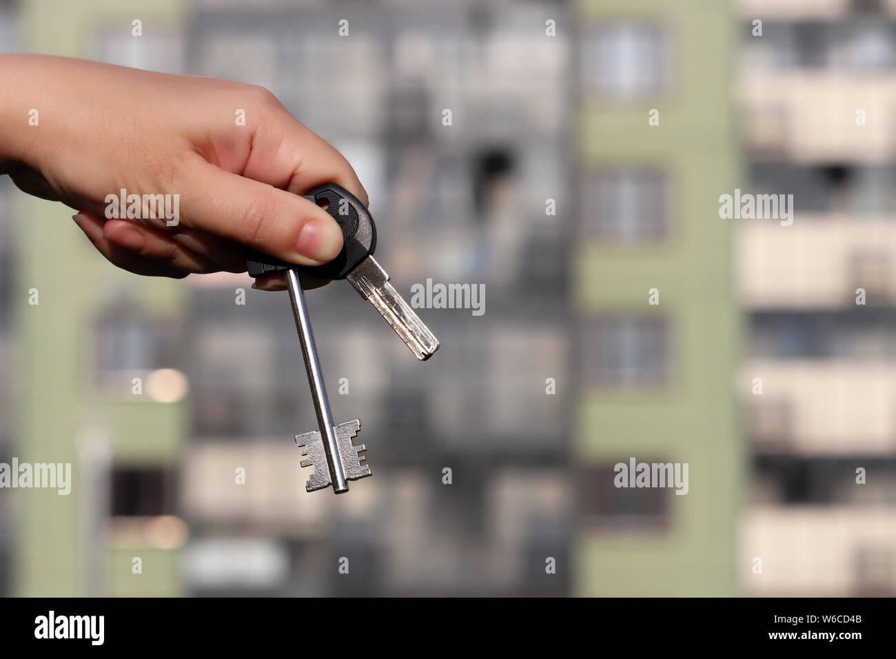 Apartment keys in hand of real estate agent on background of new residential building. Concept of house purchase, mortgage credit or rental property Stock Photo
