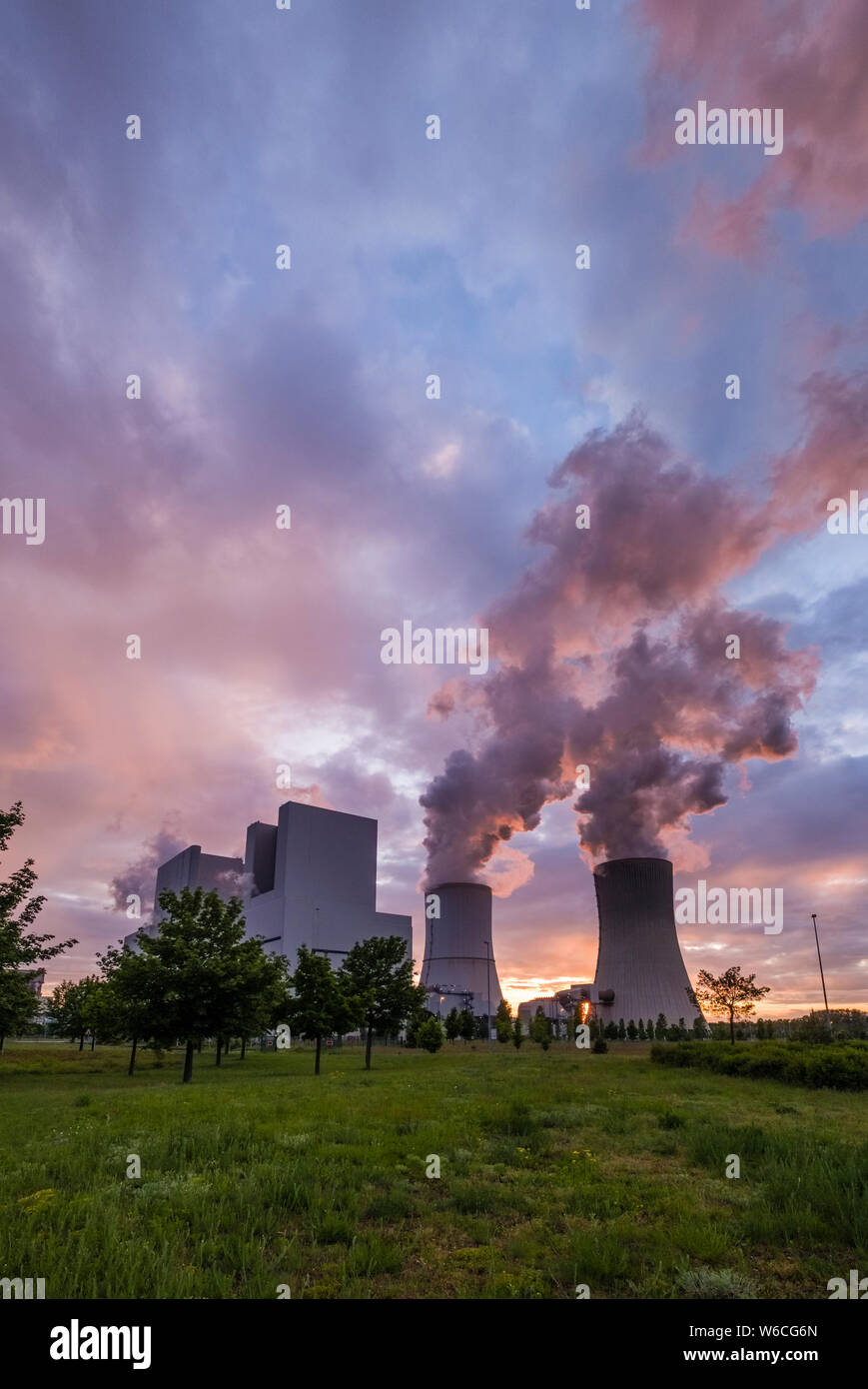 The buildings and steaming cooling towers of a coal-fired power plant in agricultural landscape at sunset Stock Photo