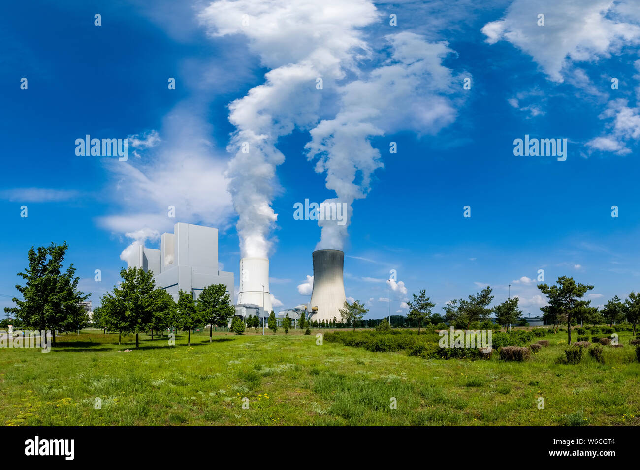 The buildings and steaming cooling towers of a coal-fired power plant in agricultural landscape Stock Photo