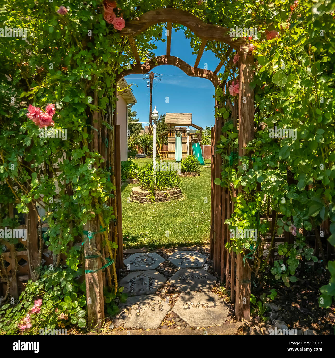 Square Arched wooden arbor at the entrance of a garden with playhouse  slides and swings Stock Photo - Alamy