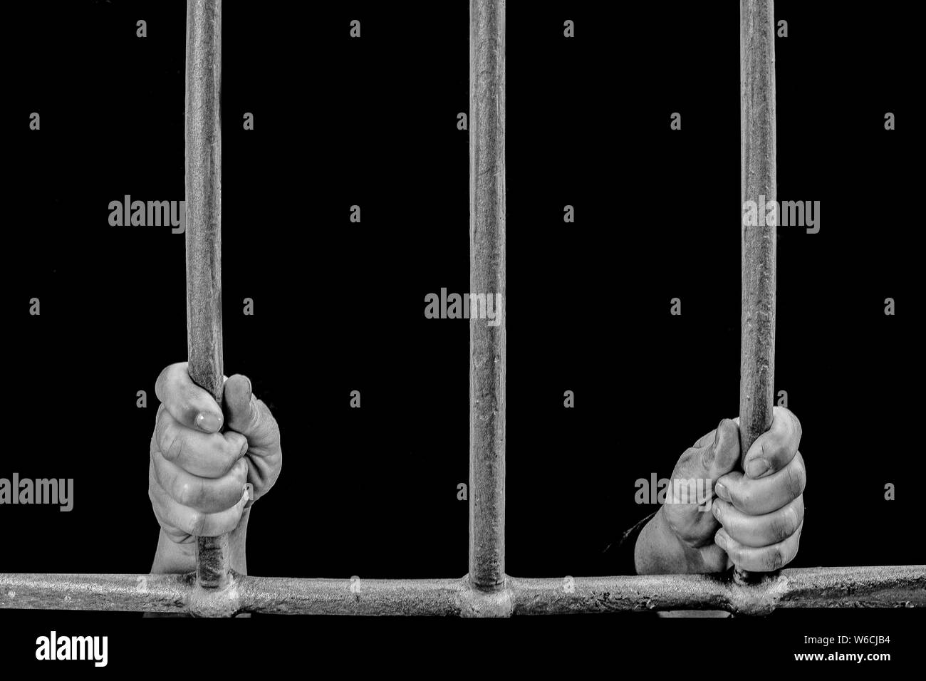 imprisoned in a dark prison holding the bars of a prison cell awaiting justice Stock Photo