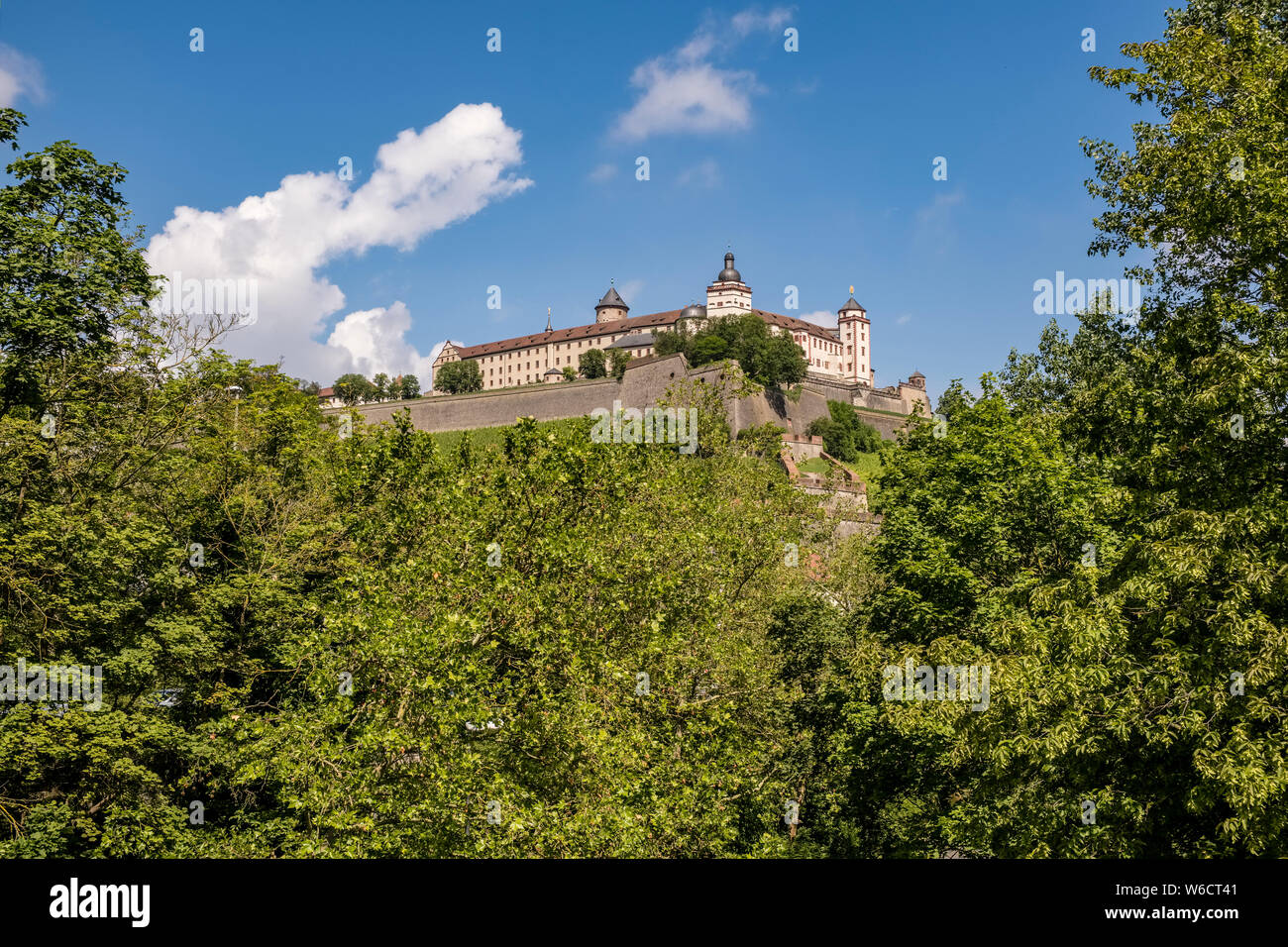 The castle Festung Marienberg is located on a hill above the town, seen through trees Stock Photo