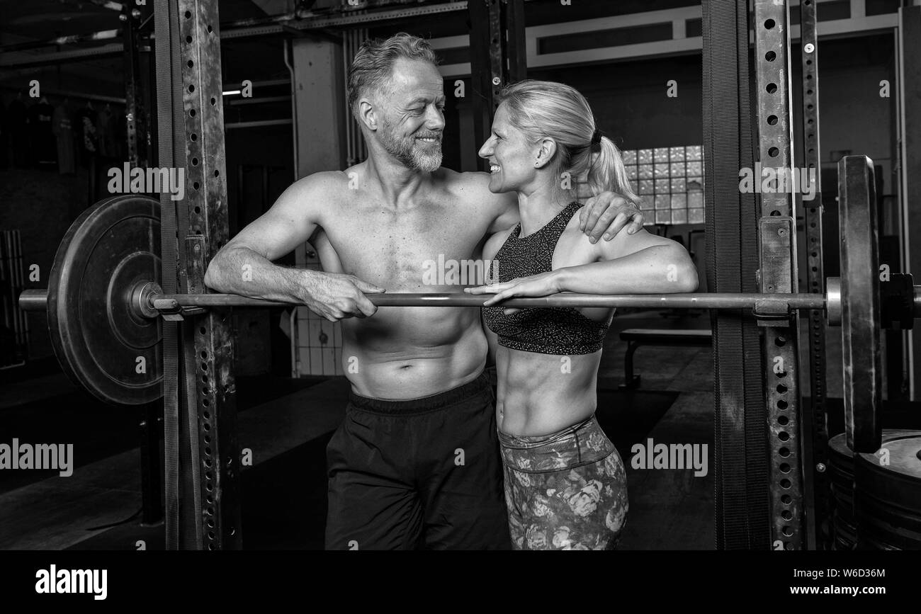 Portrait of a middle aged attractive and athletic couple who is doing a fitness training together. Strong man and woman arm in arm on the barbell. Stock Photo