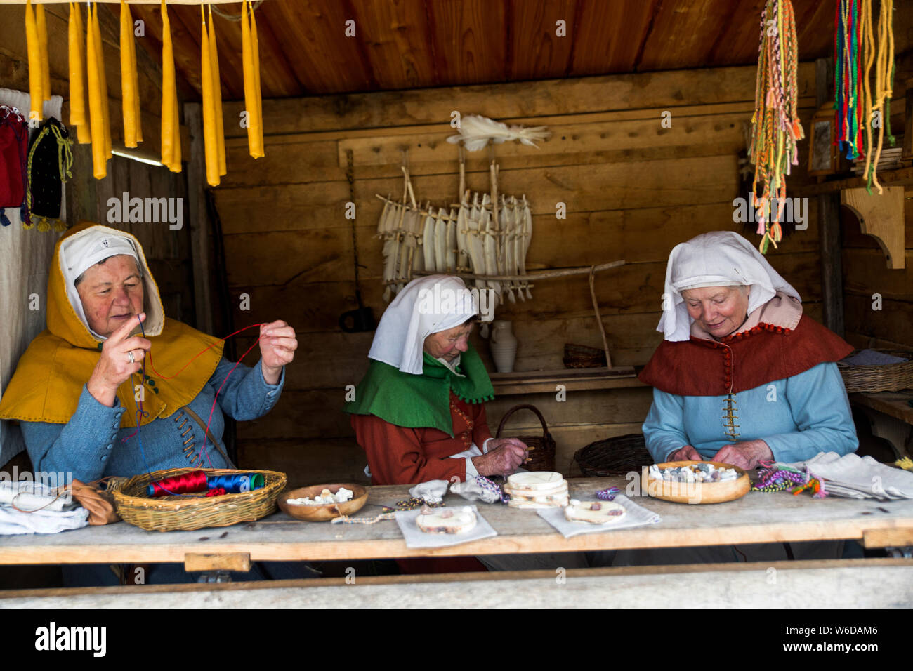 Women in traditional folk costume in a traders booth at the outdoor Medieval Centre in Nykøbing Falster, Denmark. The Medieval Centre is built around the village Sundkøbing at a fjord as it was around the year 1400. Houses are authentically designed and built with the people who populate the village, men, women, children, peasants, craftsmen, warriors and knights etc dressing and work as they would back in 1400.  Canons and large trebuchets can be seen firing missiles, knights in armour on horseback competing with lances and swords, dyers colouring textiles with plants and in the convent garde Stock Photo