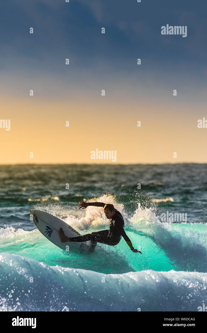 A surfer riding a wave backlit by the setting sun at Fistral in Newquay in Cornwall. Stock Photo