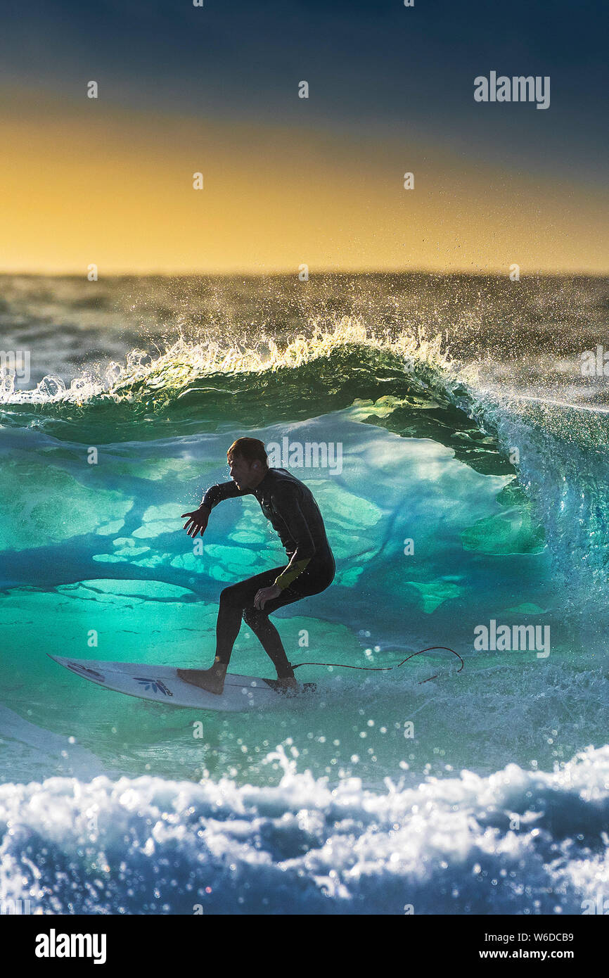 A surfer riding a wave backlit by the setting sun at Fistral in Newquay in Cornwall. Stock Photo