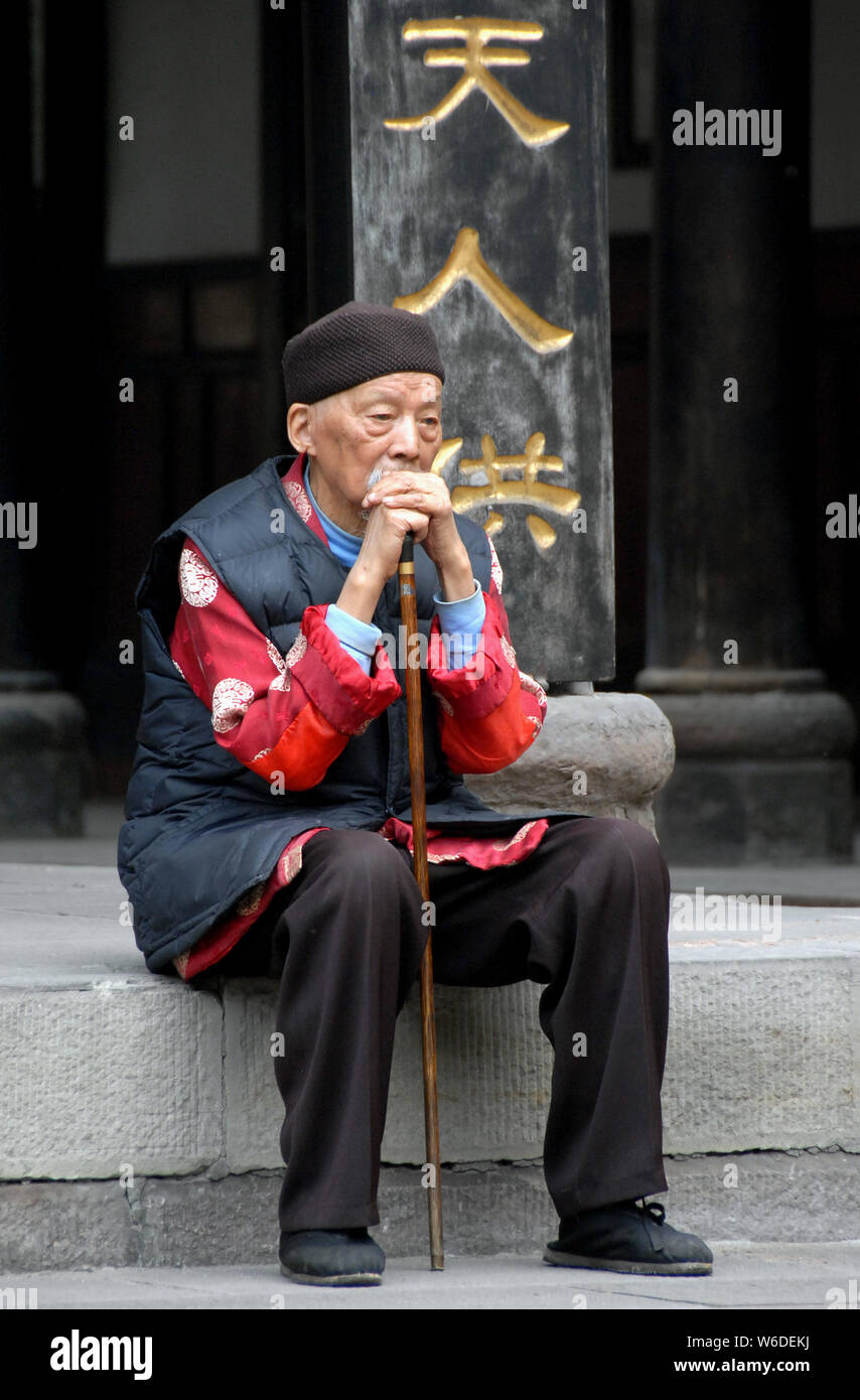 An old Chinese man sits on a stone step and meditates at Wenshu Temple in Chengdu, China. This Buddhist temple is also known as Wenshu Monastery. Stock Photo