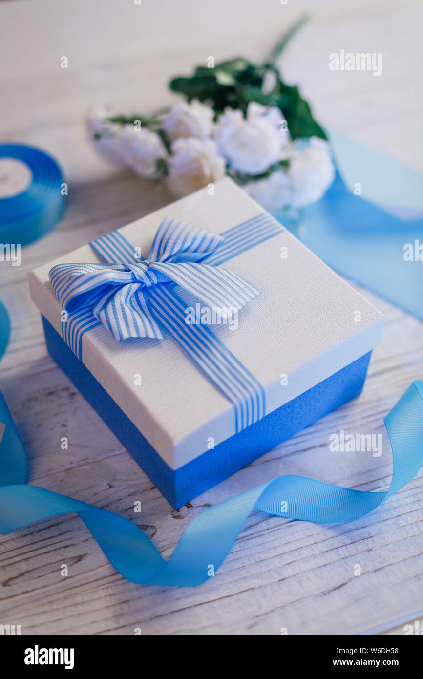 Gift box with bow. Blue satin ribbons and leaf sconces. Flowers in the background. Stock Photo