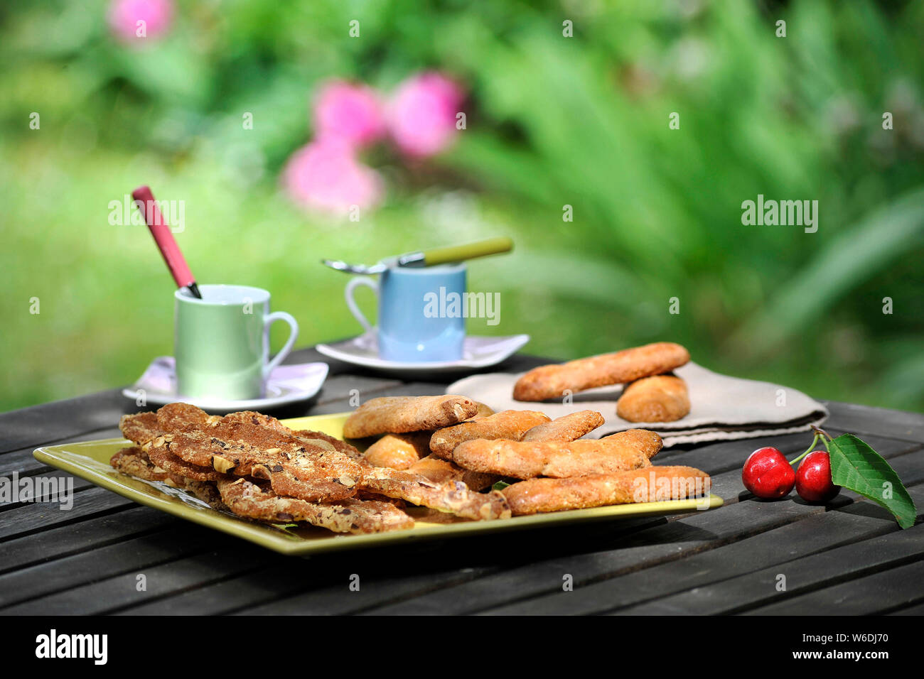 Table with biscuits, cups of coffee and cherries. Culinary specialties from the Berry area: almond “croquets” biscuits from Berry and coffee, in a gar Stock Photo